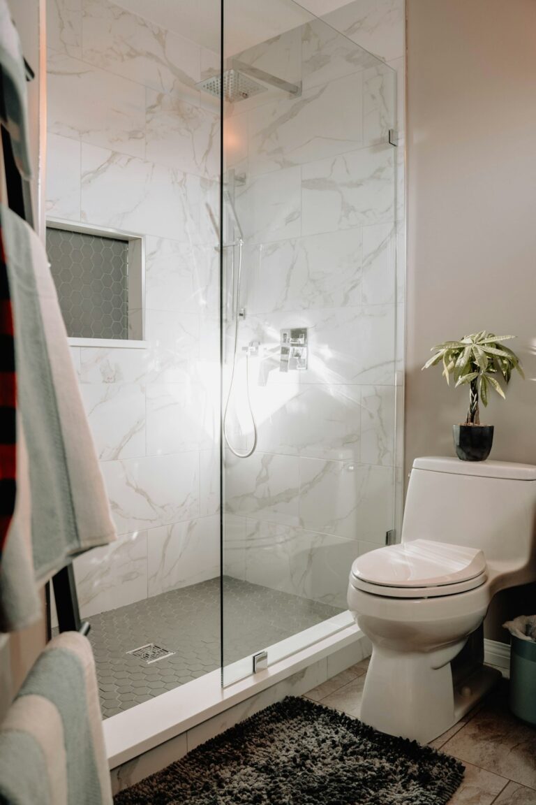 Person cleaning bathroom tile grout with gloves, a scrub brush, and white vinegar in a spray bottle.